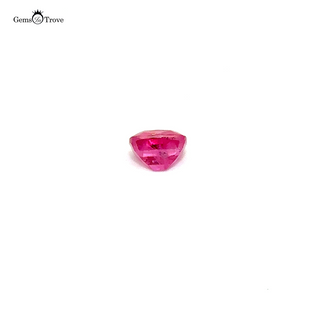 A loose pinkish ruby gemstone resting on a white turntable, reflecting soft light.