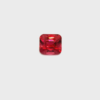A rotating Mahenge spinel gemstone on a white turntable, highlighting its vivid reddish-pink brilliance.