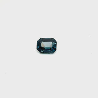 A 1.54ct deep blue, emerald-cut sapphire on white turn table, reflecting its rich color and fine clarity.